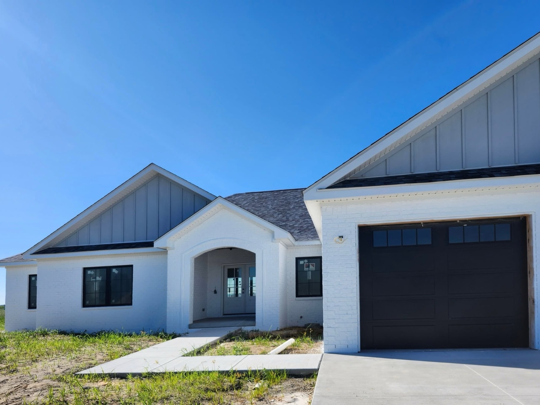 Bright white painted-brick home with black windows, gray board-and-batten gables and a dark garage door